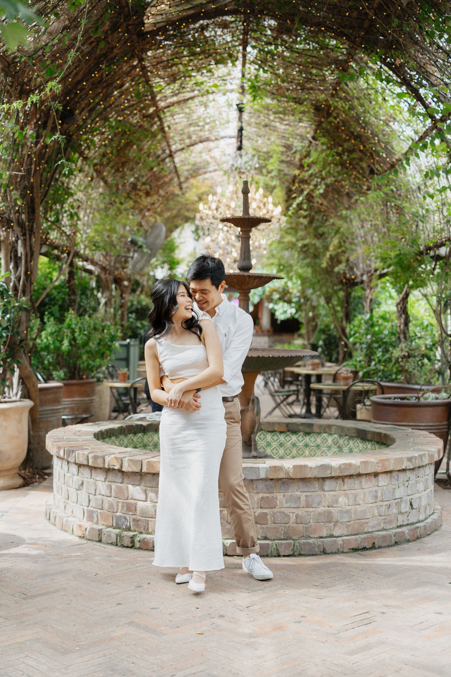 Wedding couple poses under vine-covered archway in romantic garden setting.