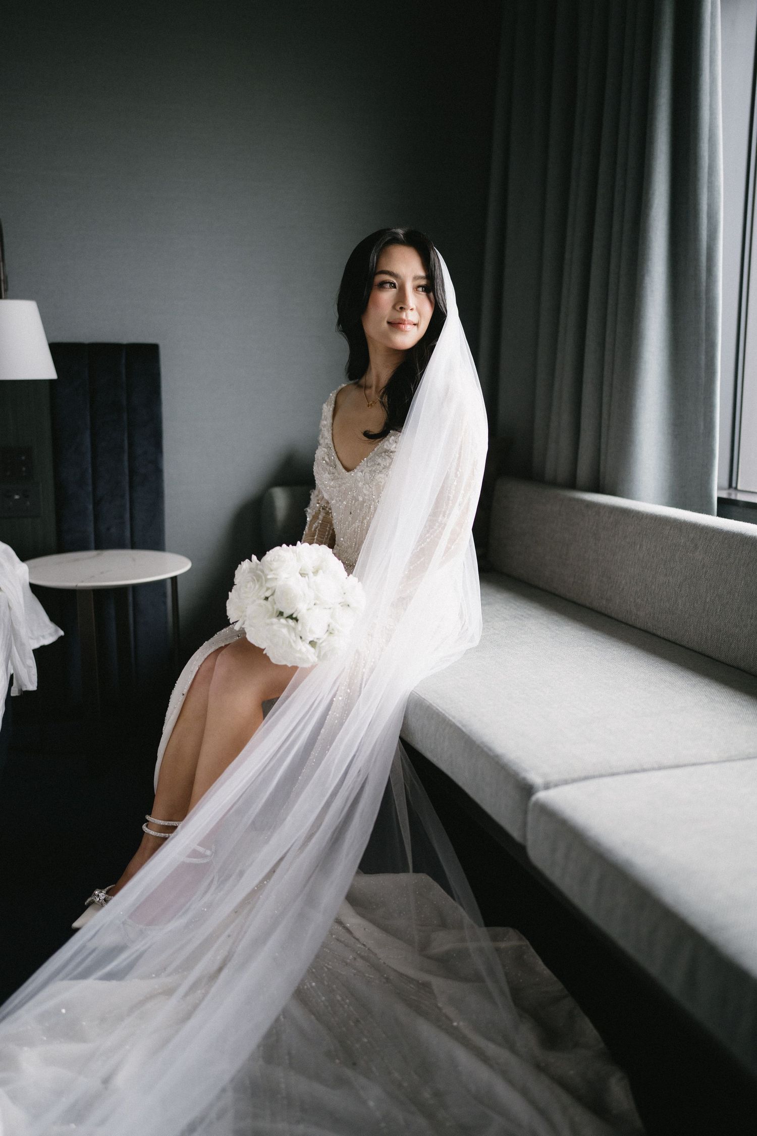 A person in a white lace dress poses gracefully with flowing white fabric in a minimalist interior setting.