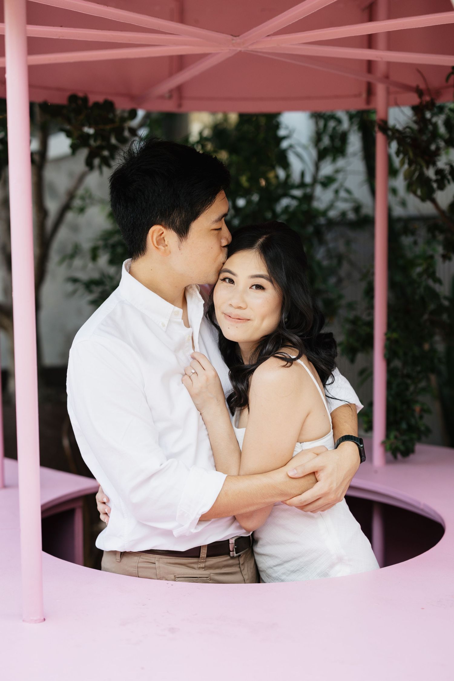 Romantic couple sharing tender moments in a pink-hued pavilion setting.