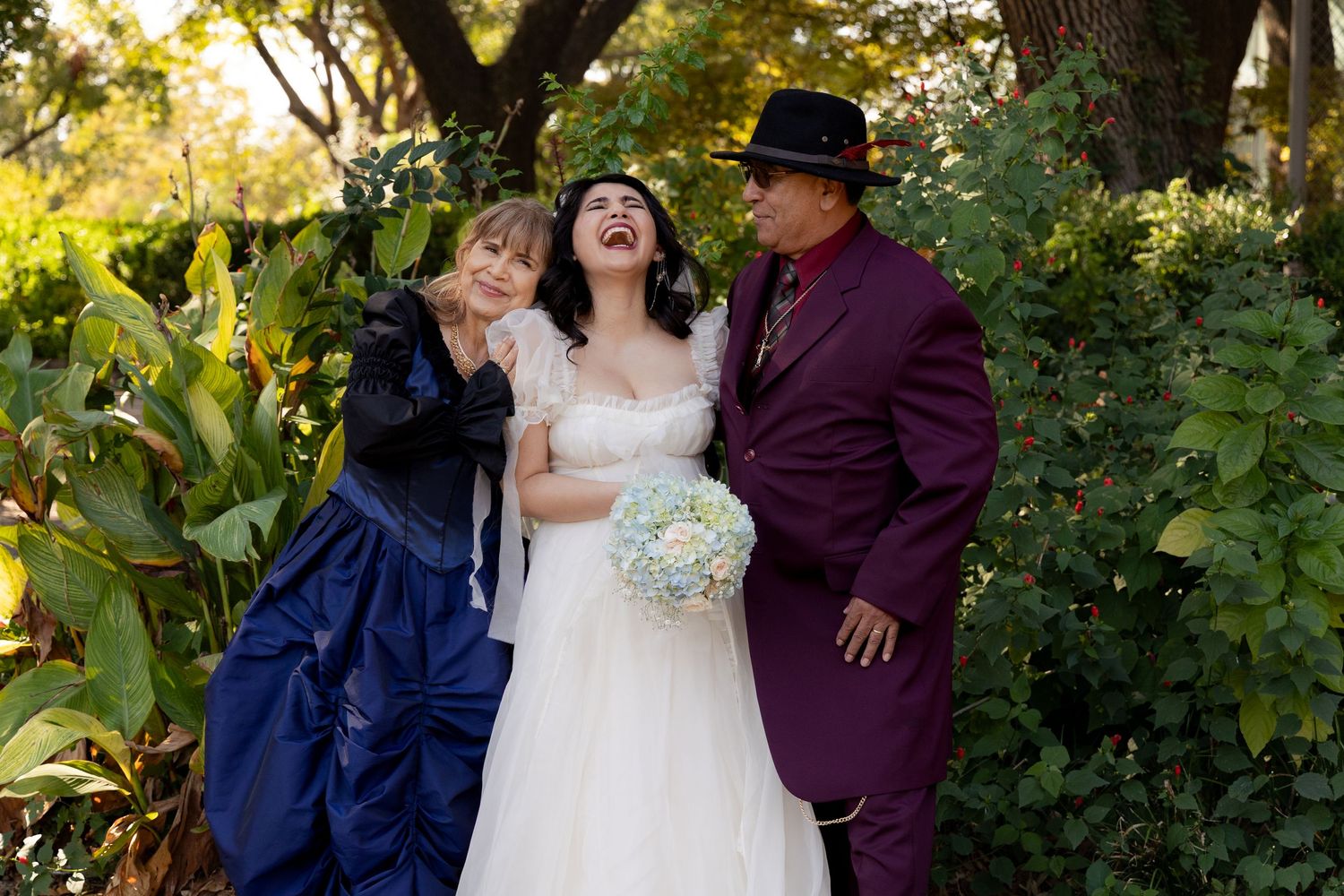 A couple shares romantic outdoor wedding photos in a garden setting with sunlit greenery as their backdrop.