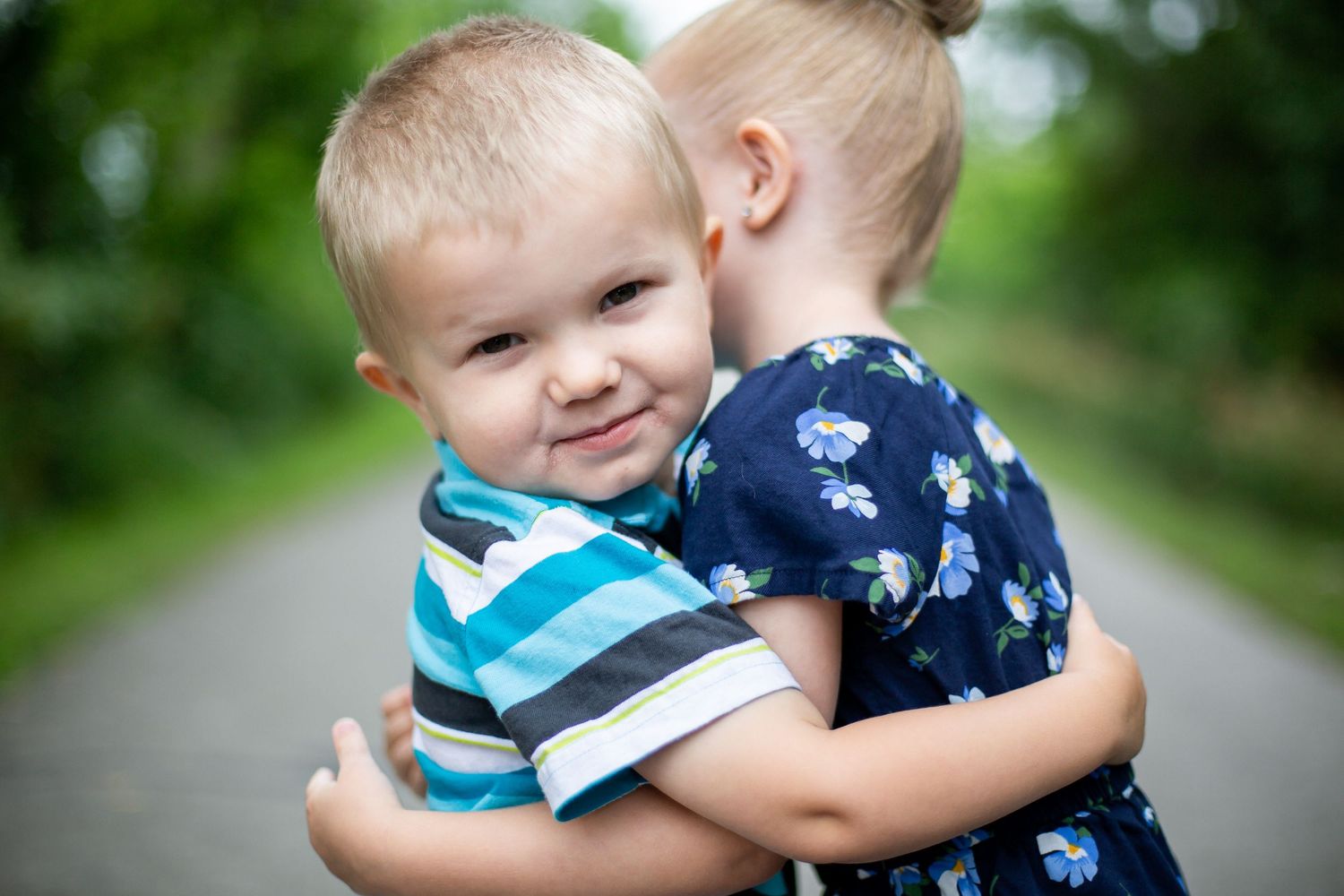 A little boy hugs his older sister in an outdoor setting