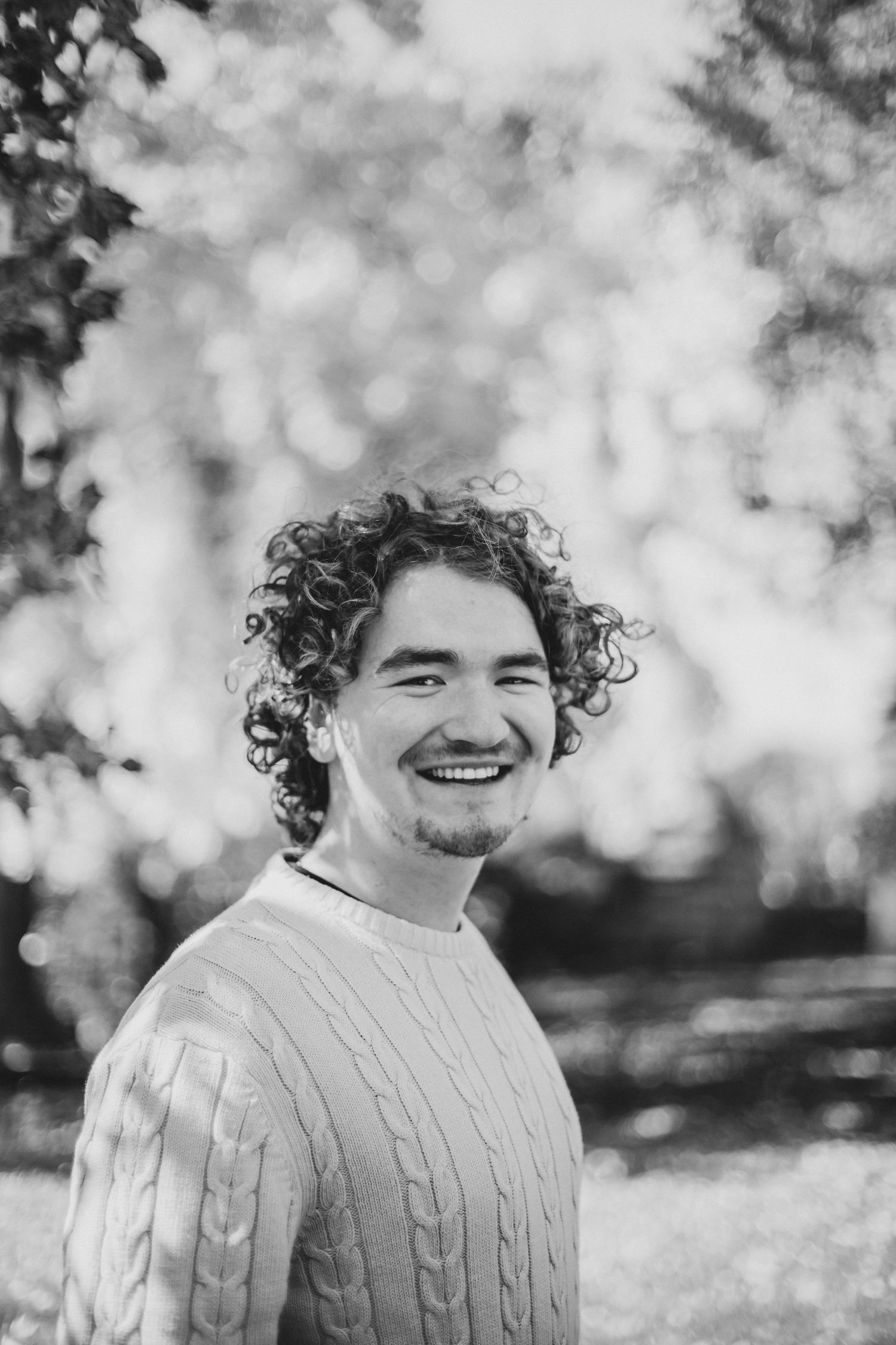 A young man with curly hair smiling in an outdoor setting