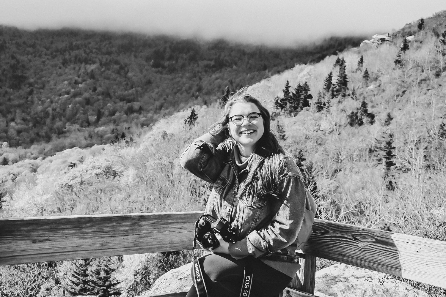 Jess Severt with a camera smiling in the mountains