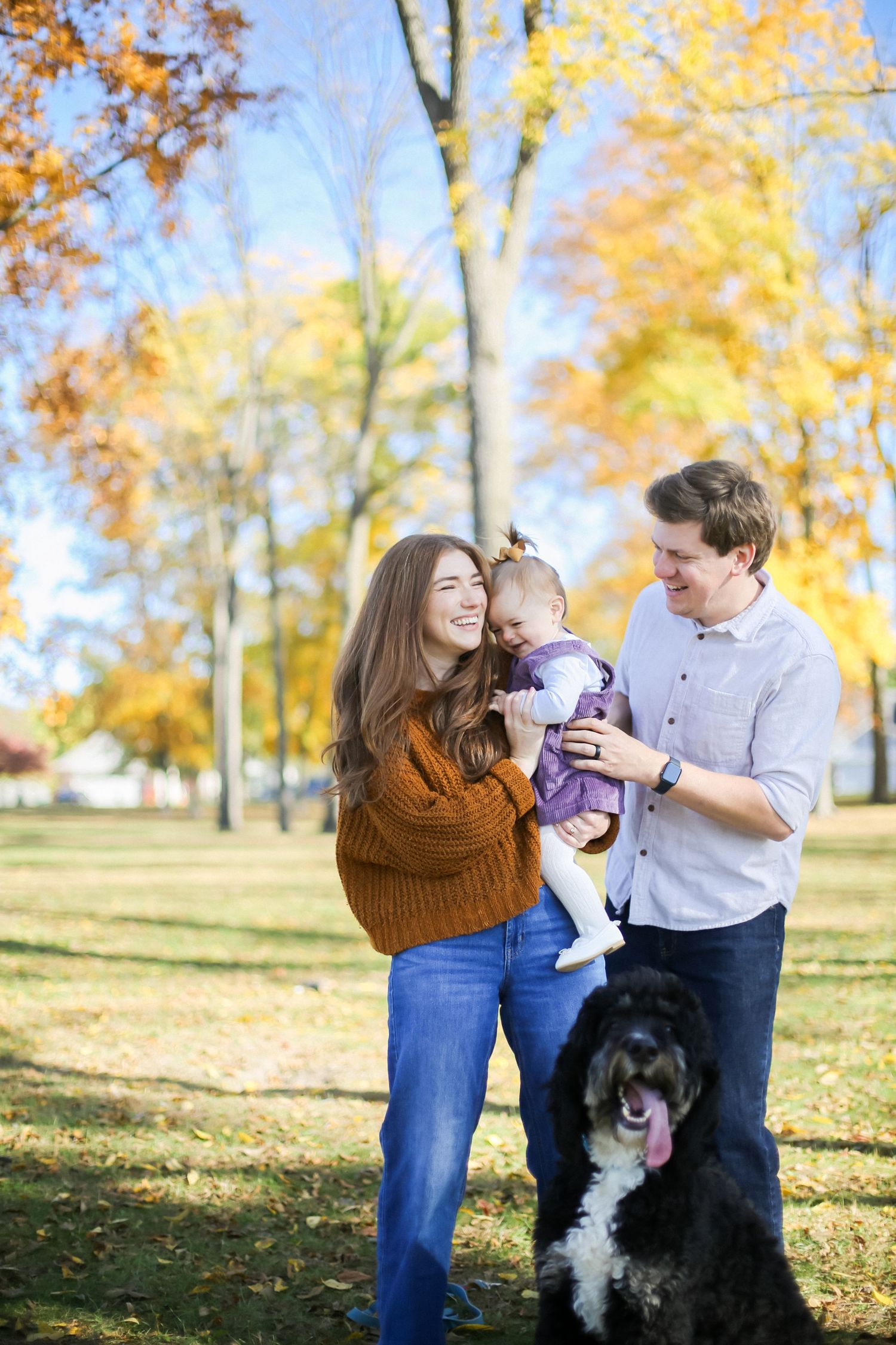 A family of parents, a daughter, and a dog laugh in a nature setting