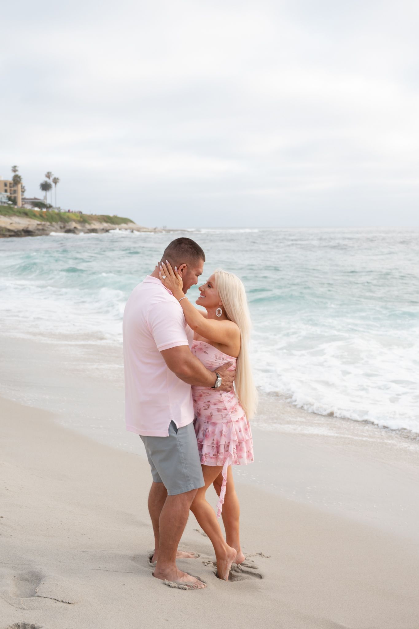 Couple embracing face to face on a sandy beach with turquoise waves in the background.