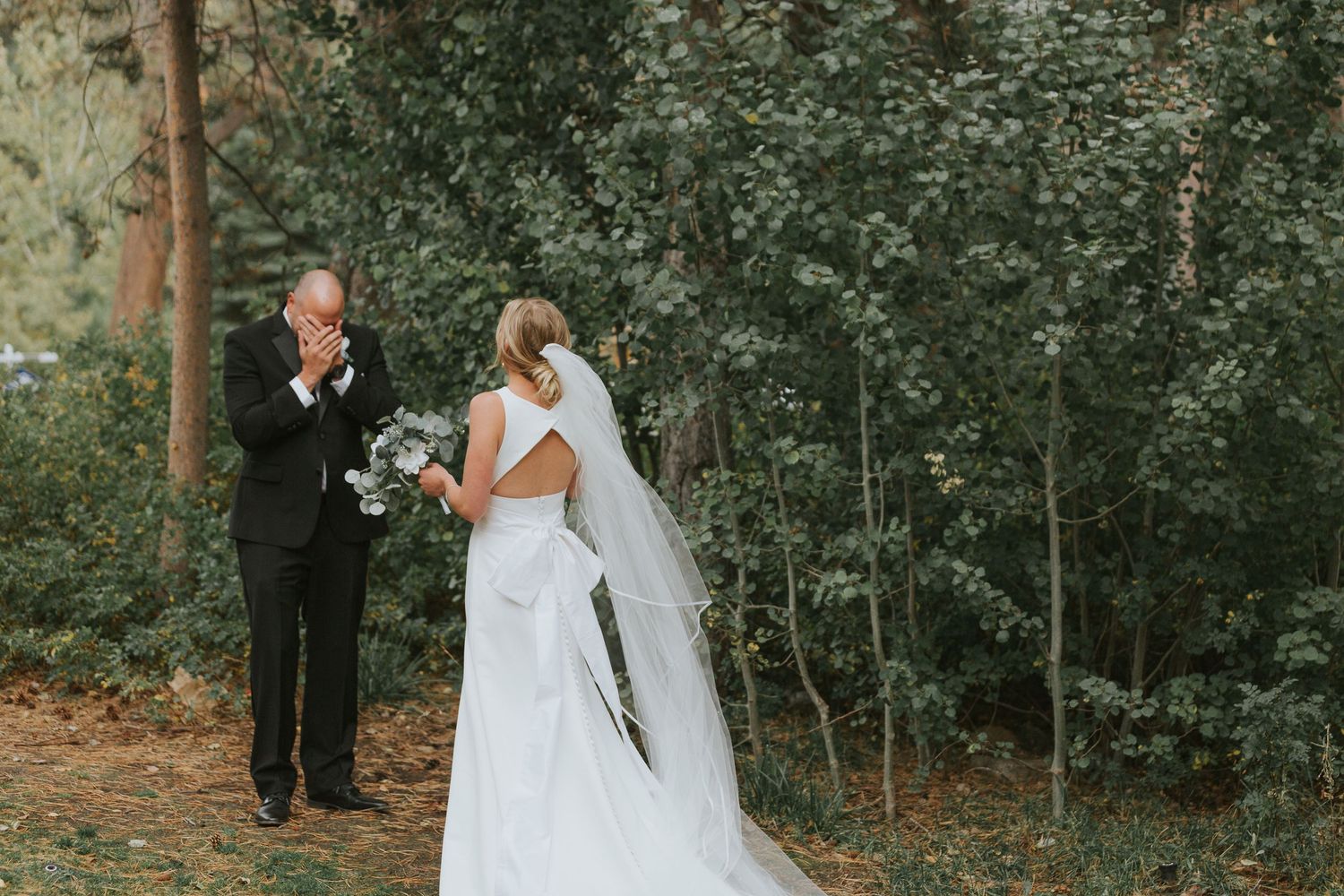 Wedding couple walking together on a forest path surrounded by green trees.