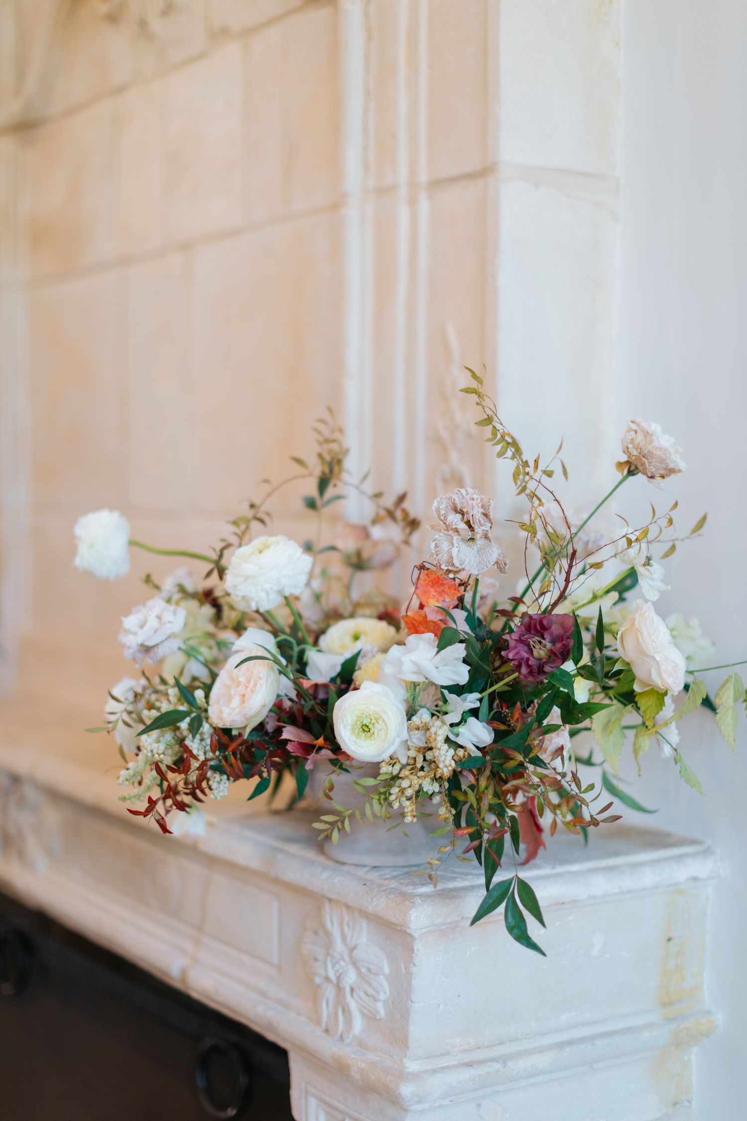 Elegant floral arrangement with roses and mixed flowers on white marble mantel.
