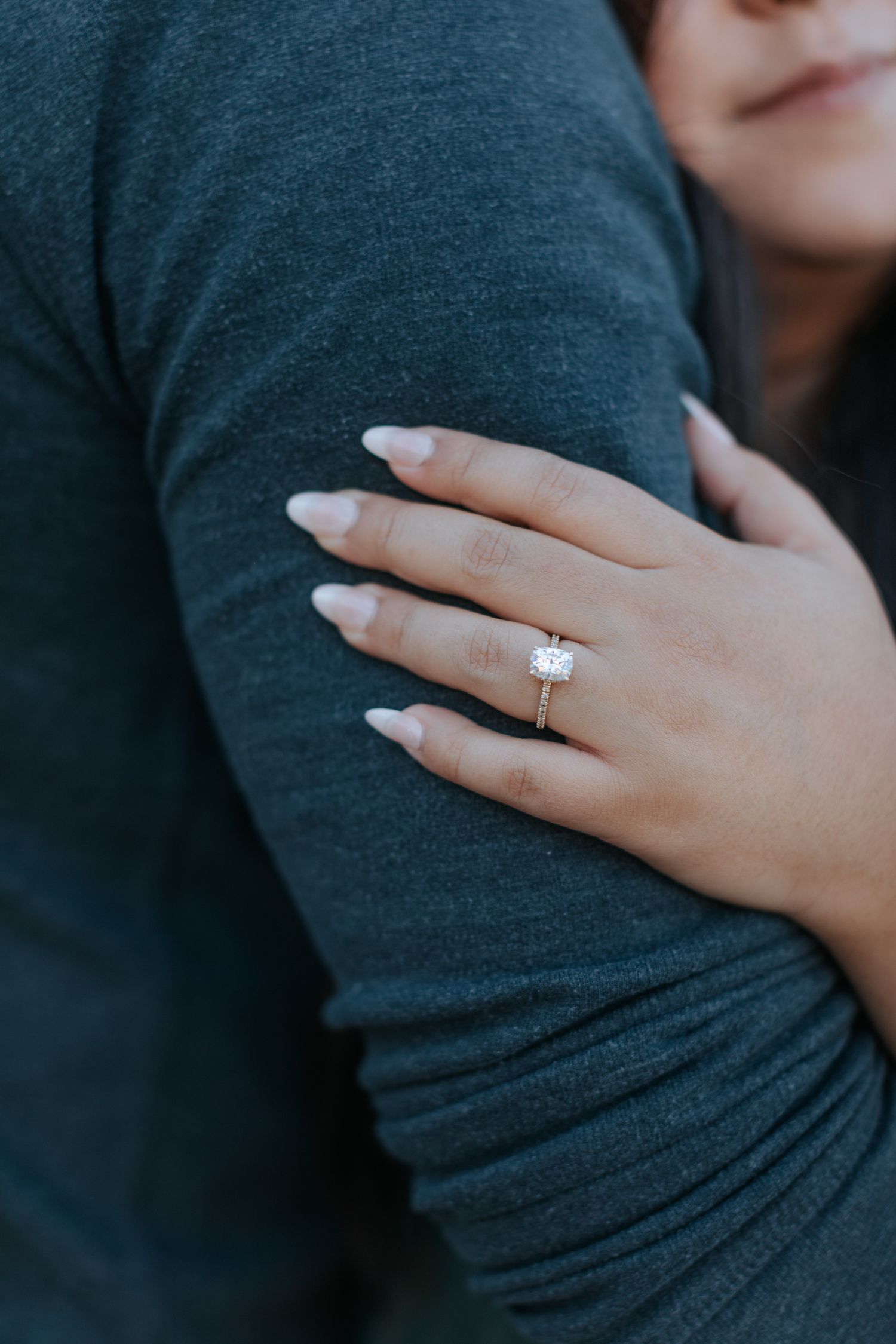 Close-up shots of a sparkling engagement ring on a hand against a dark shirt.