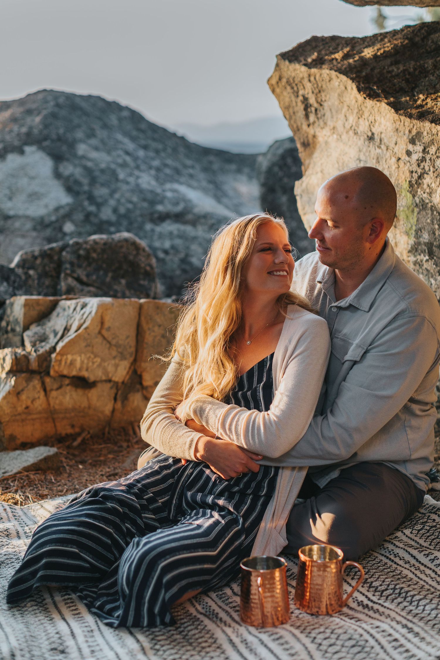 Couple relaxes on a blanket against rocky cliffs during an intimate outdoor photoshoot.