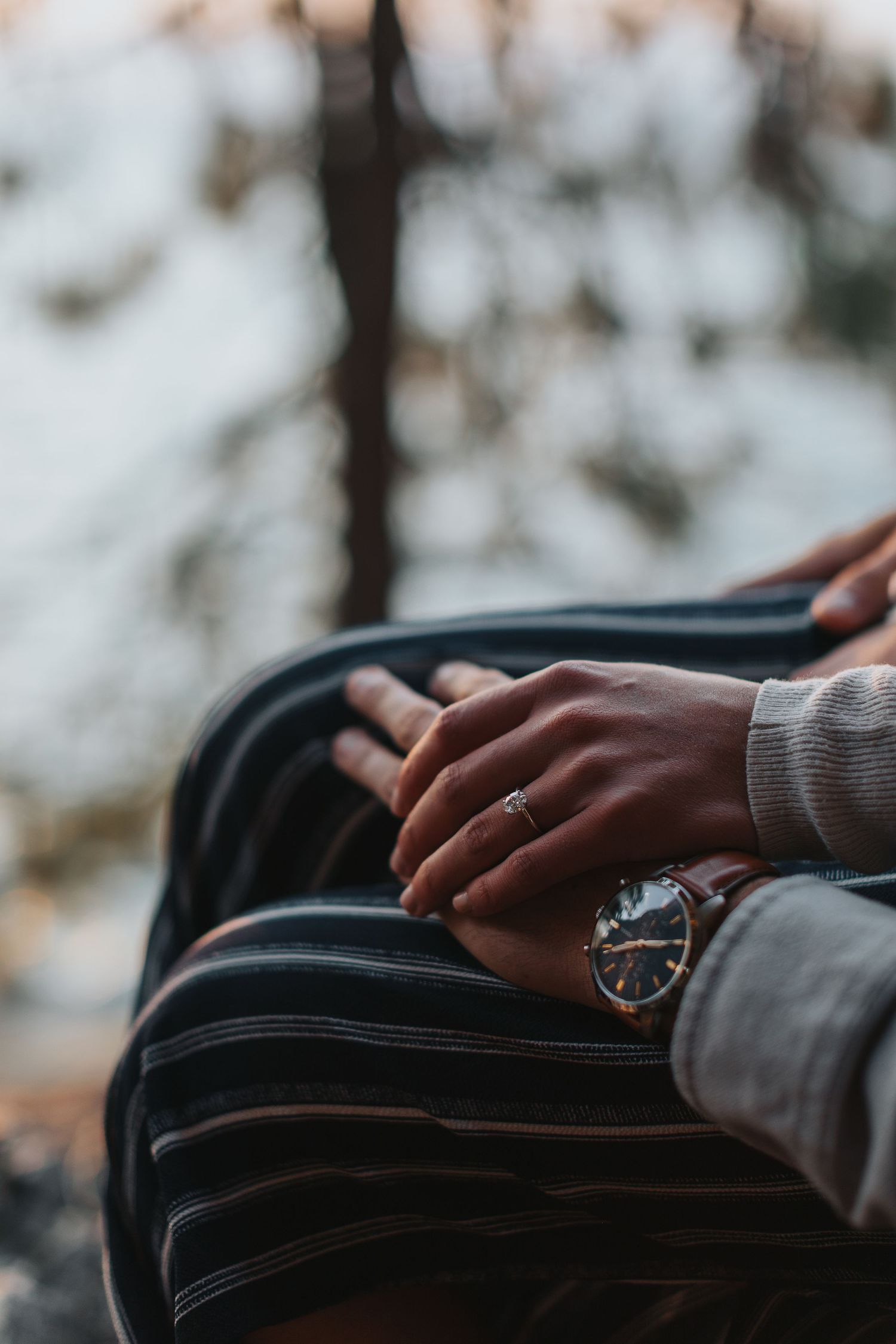 Close-up shot of hands touching a black leather bag against a blurred natural background.