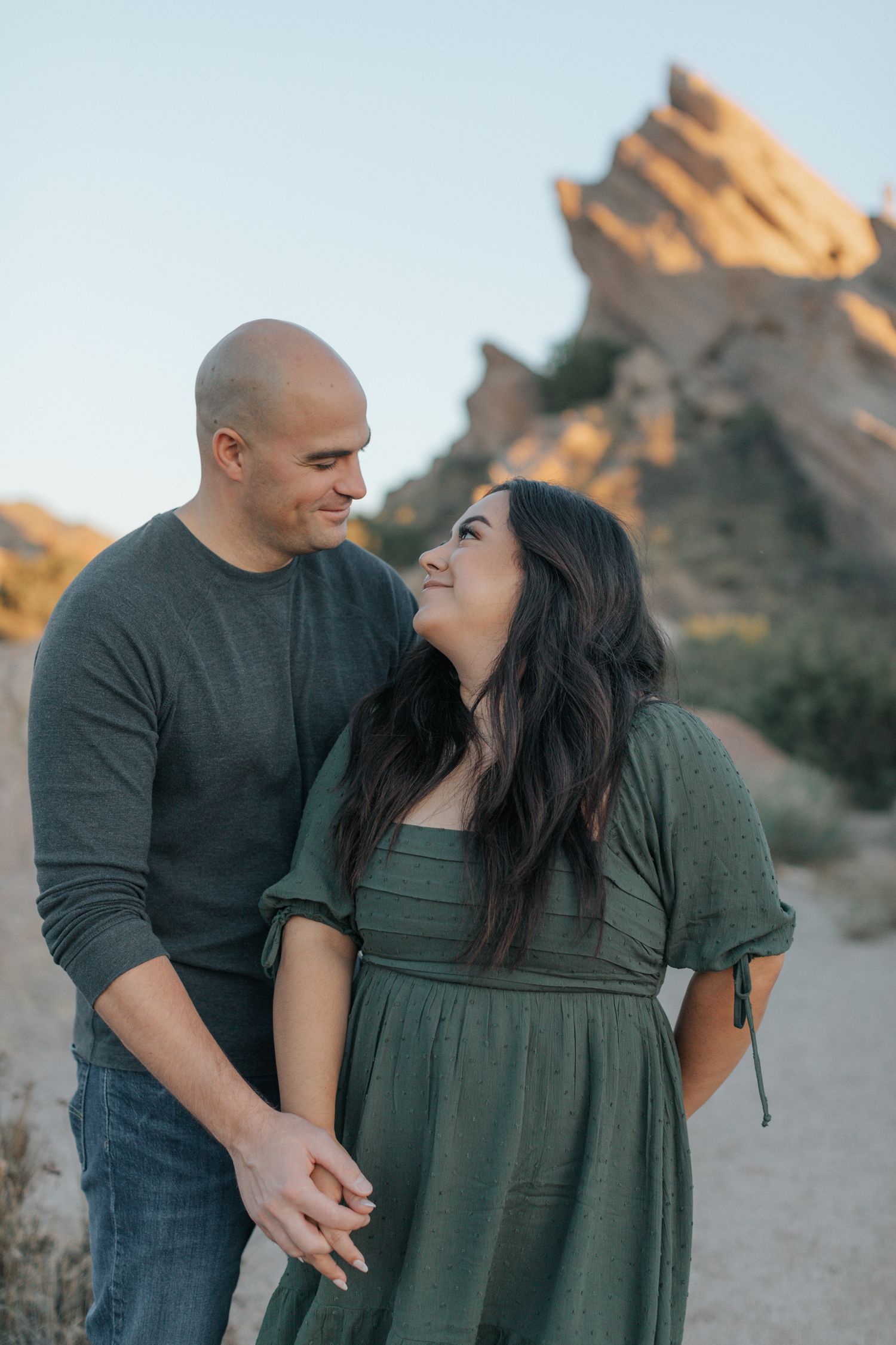 A couple shares an intimate moment against a backdrop of rocky desert cliffs at sunset.