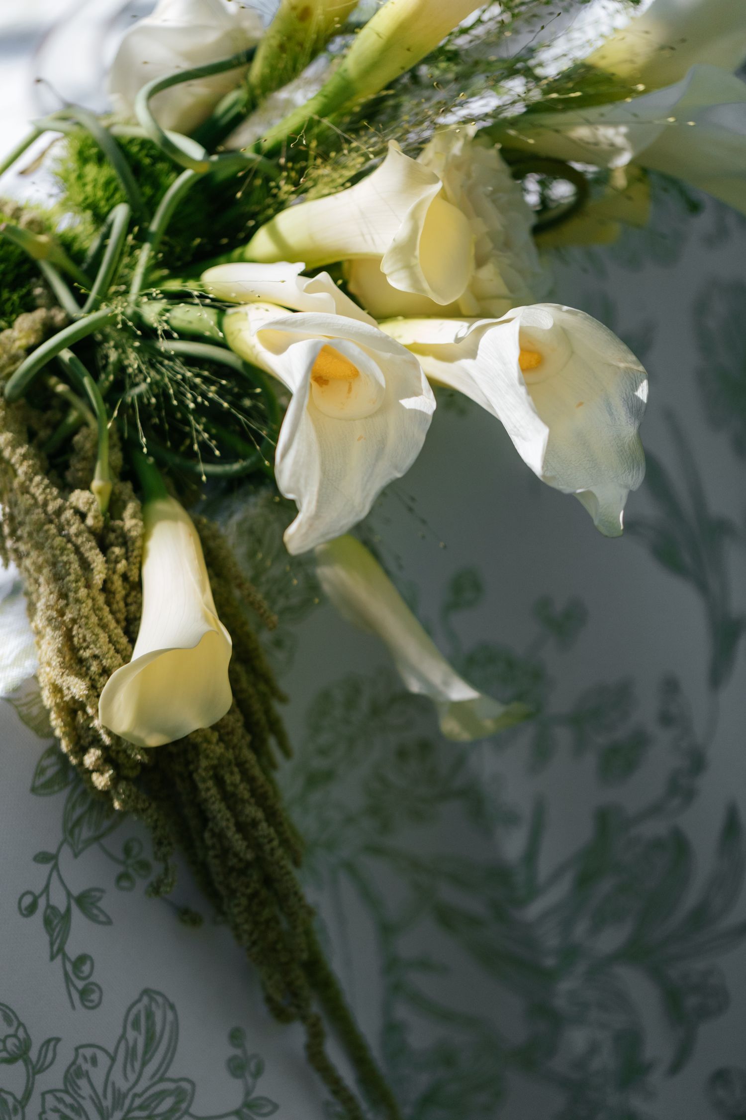 Elegant white calla lilies and greenery arranged in a wedding bouquet against a textured background.