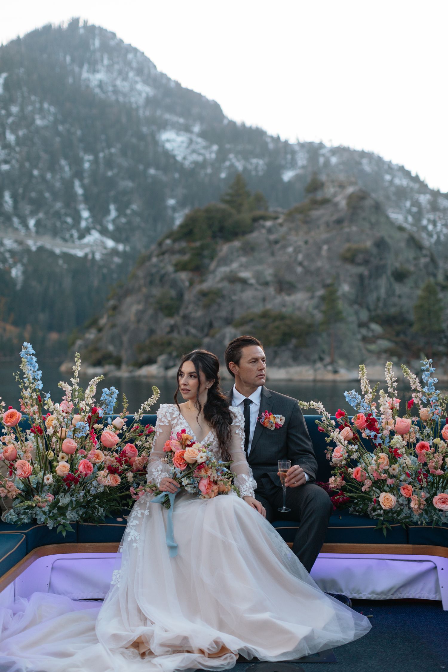 A couple sits on a boat deck surrounded by lush floral arrangements with snowy mountains in the background.