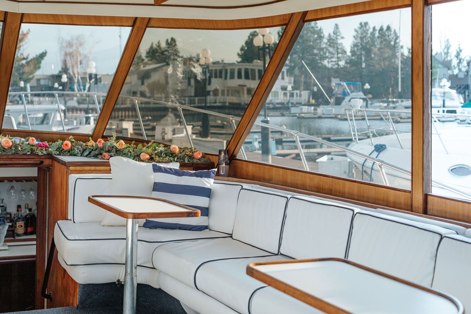 Panoramic view of yacht interior showing white bench seating and large windows overlooking marina.