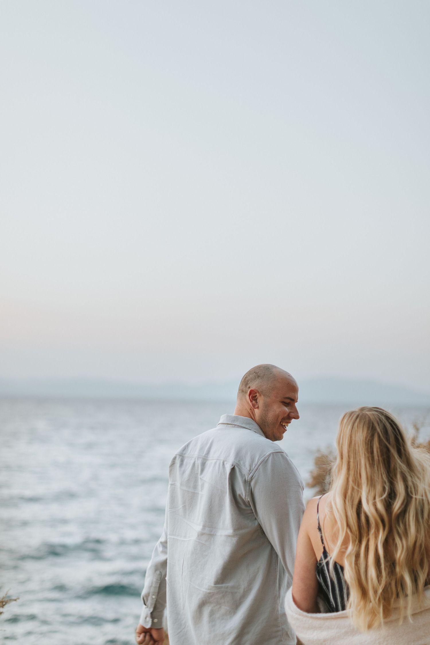 Couple stands together overlooking the ocean during golden hour.