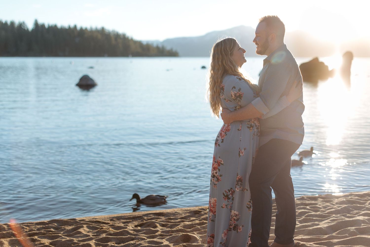 Sunset engagement photography session on a lakeside beach with golden hour lighting.