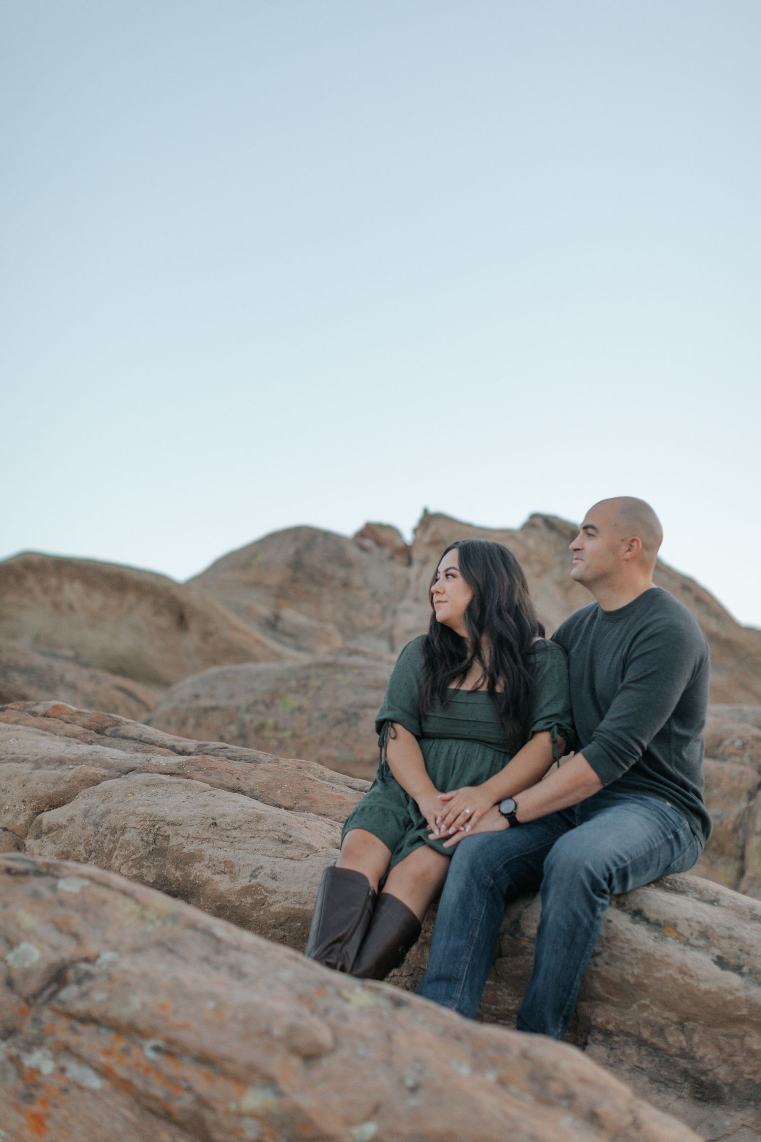 A couple sits together on rocky terrain during a desert photoshoot at sunset.