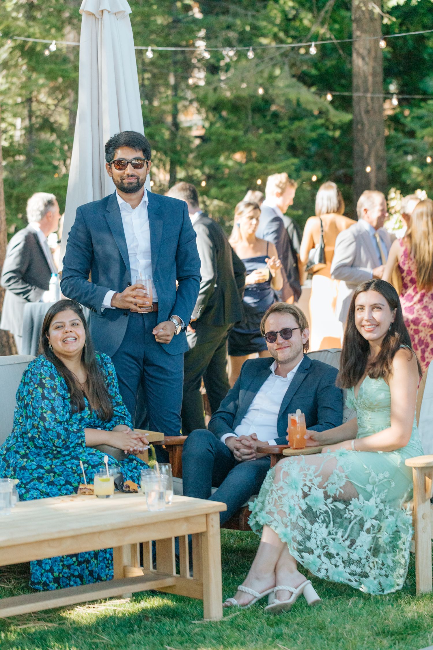 Wedding guests relaxing on wooden benches during an outdoor garden reception.