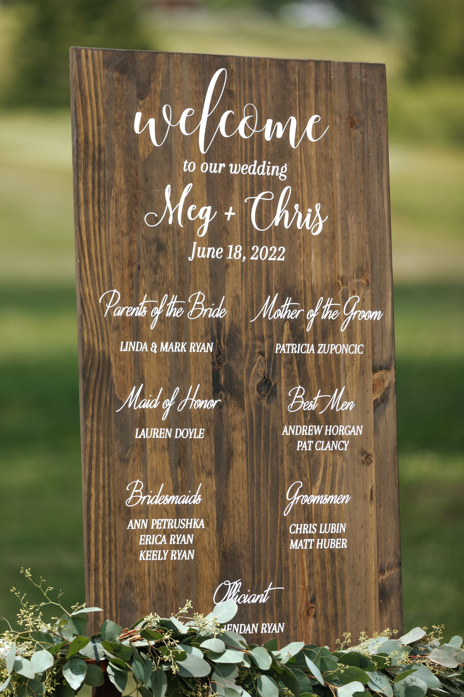 Rustic wooden wedding welcome sign displays bridal party names and wedding date.