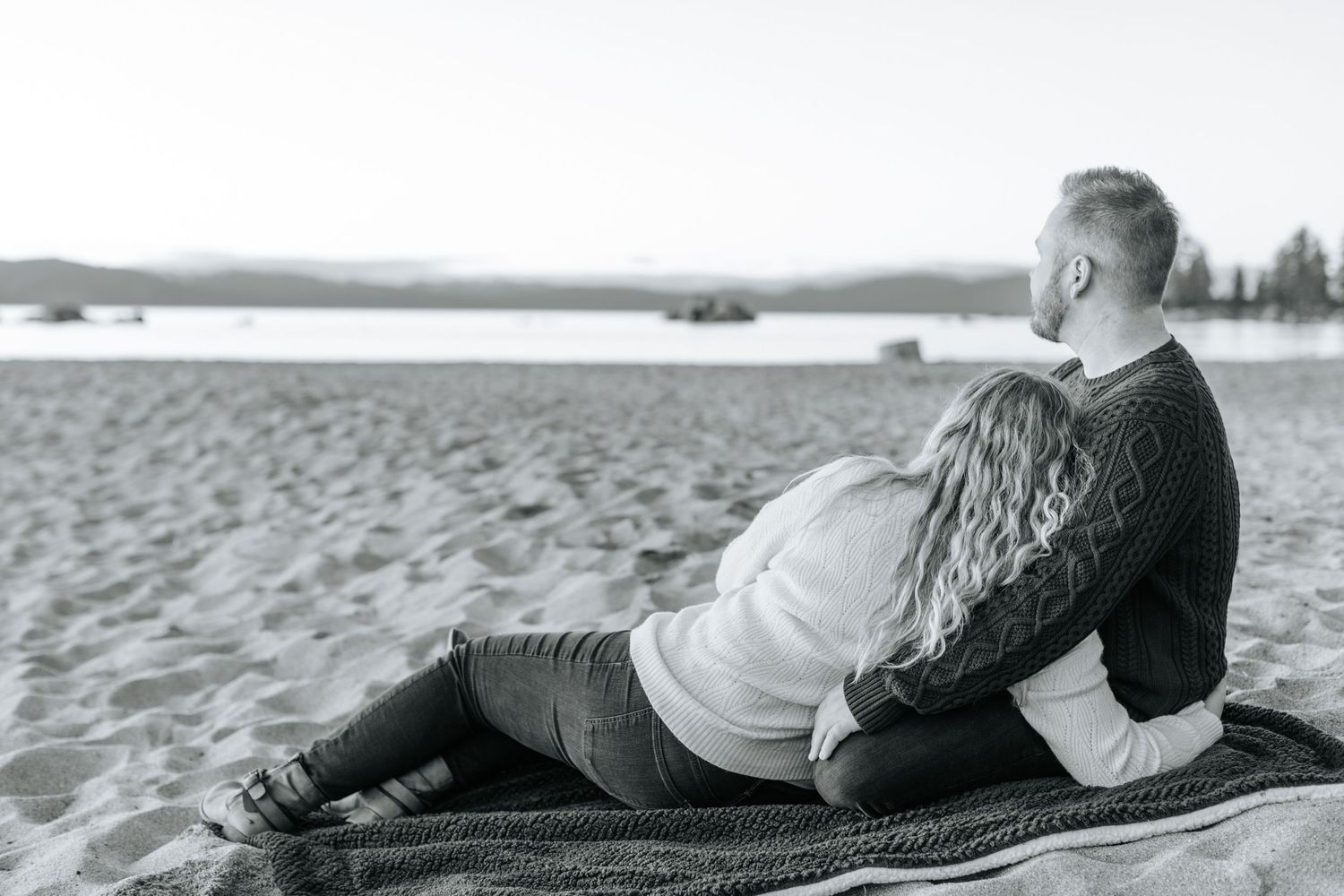 Black and white photo series of a couple lying on a beach blanket near the water.