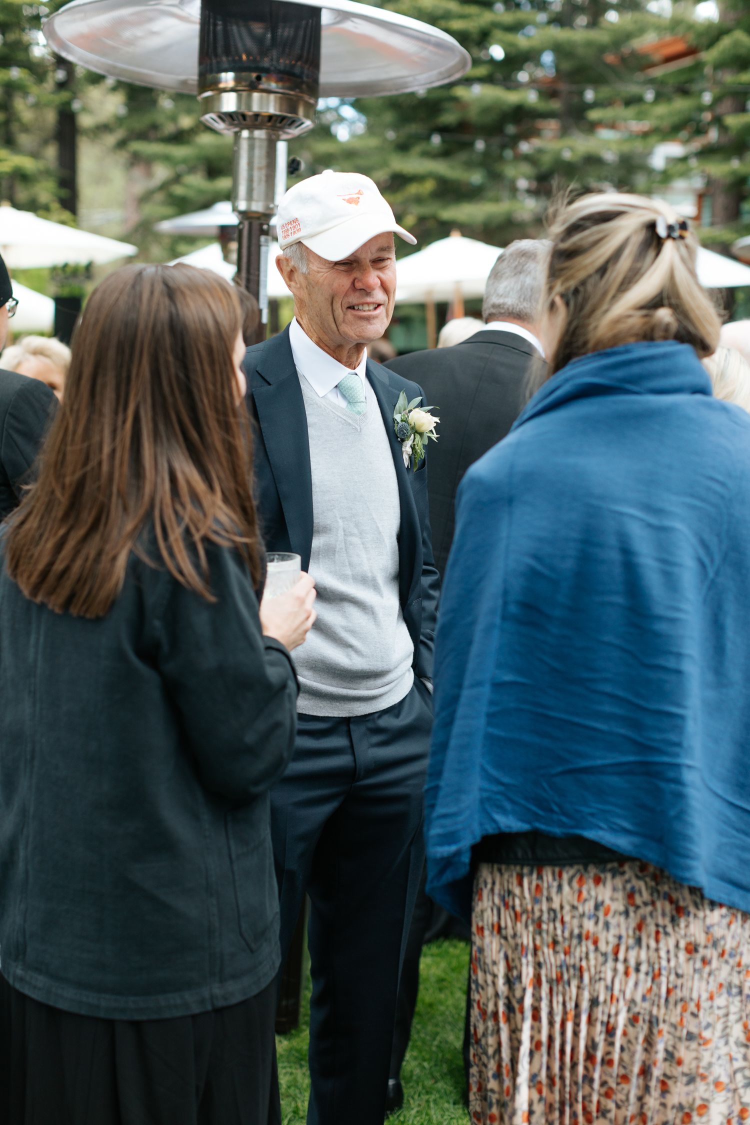 Wedding guests mingle during outdoor reception under white tent canopy.
