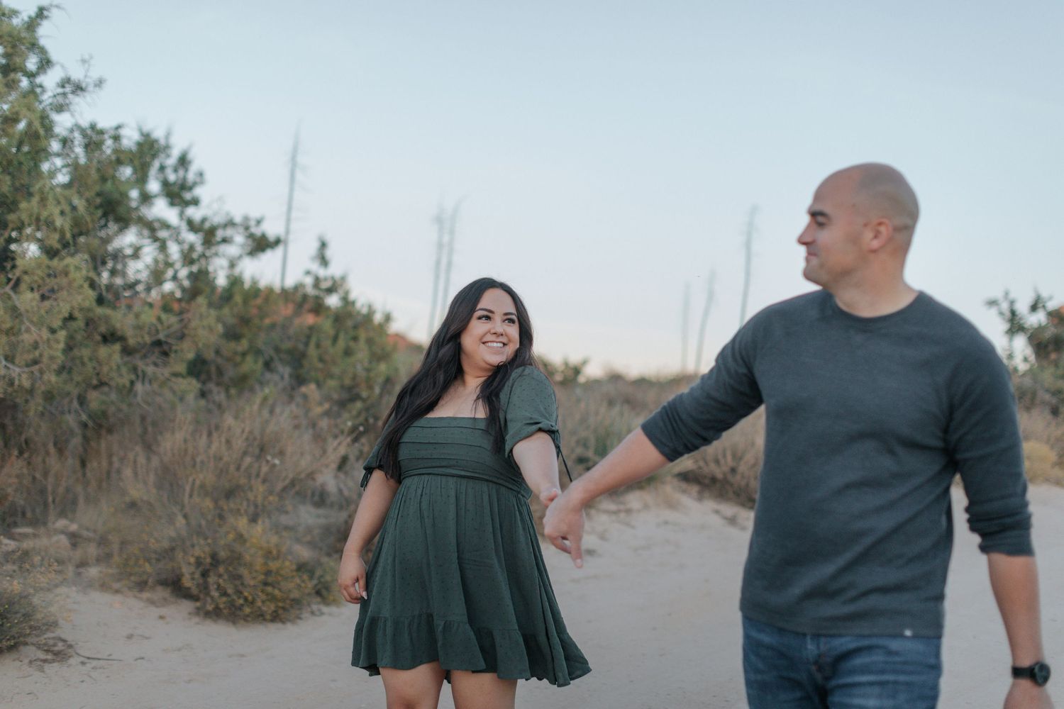 Couple walking and embracing on desert path with mountains in background.