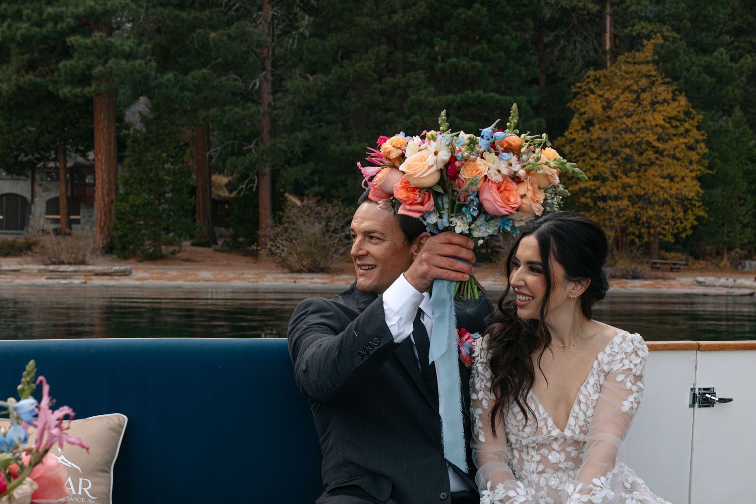 Couple sharing joyful moment on boat with colorful floral arrangements and lake backdrop.
