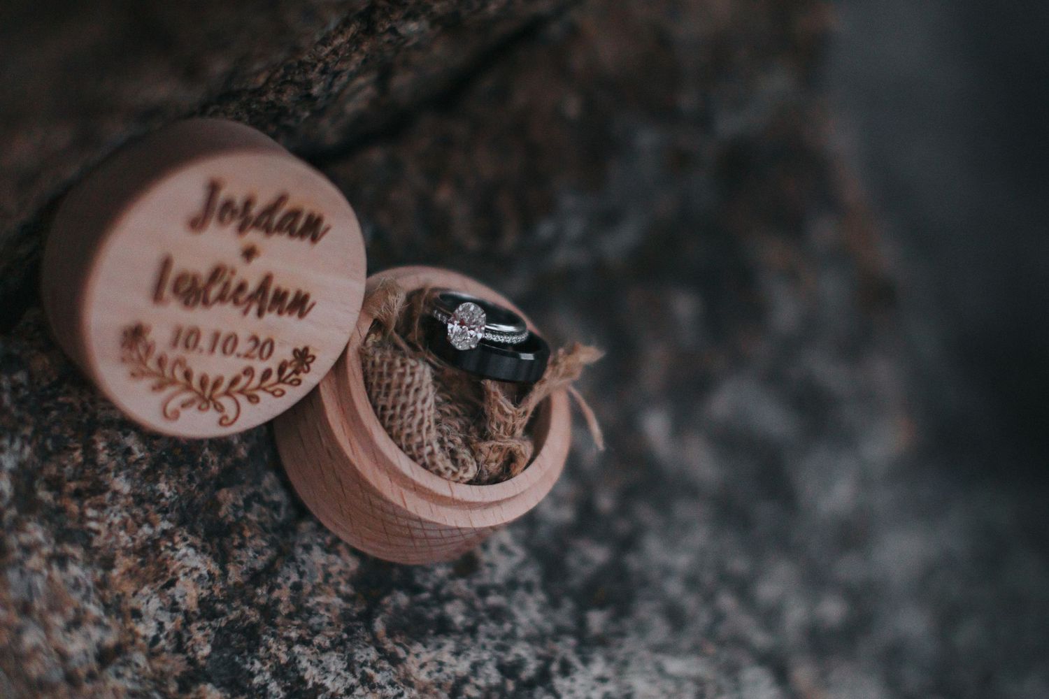 Wedding rings displayed on dark textured stone in moody lighting.
