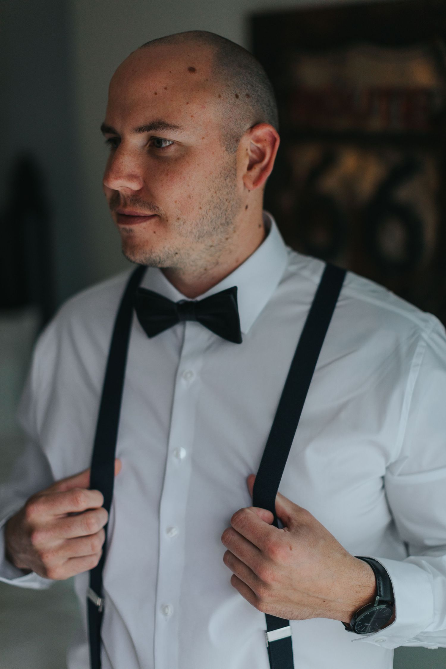 Person adjusting black suspenders over a crisp white dress shirt.