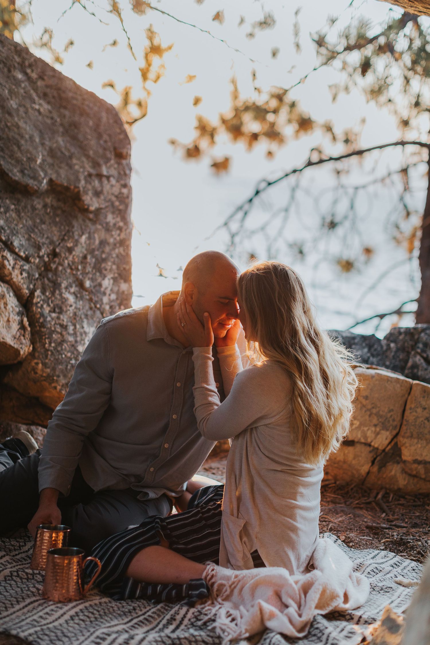 Romantic couple sitting on rocks during golden hour with autumn foliage in the background.