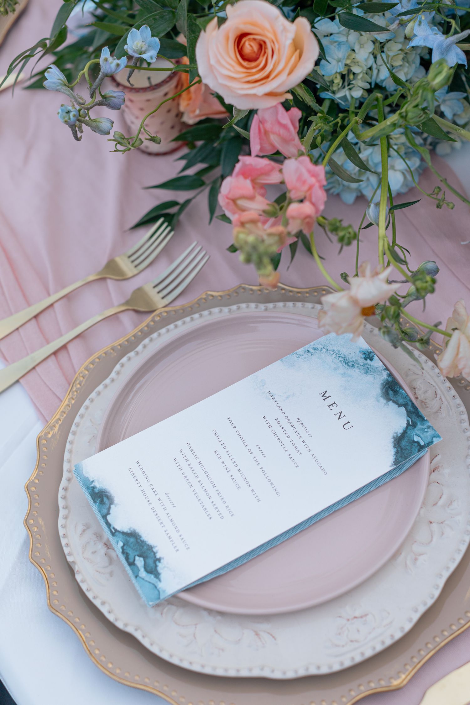 Elegant place setting with pink plates, floral arrangements and menu card in soft pastel colors.