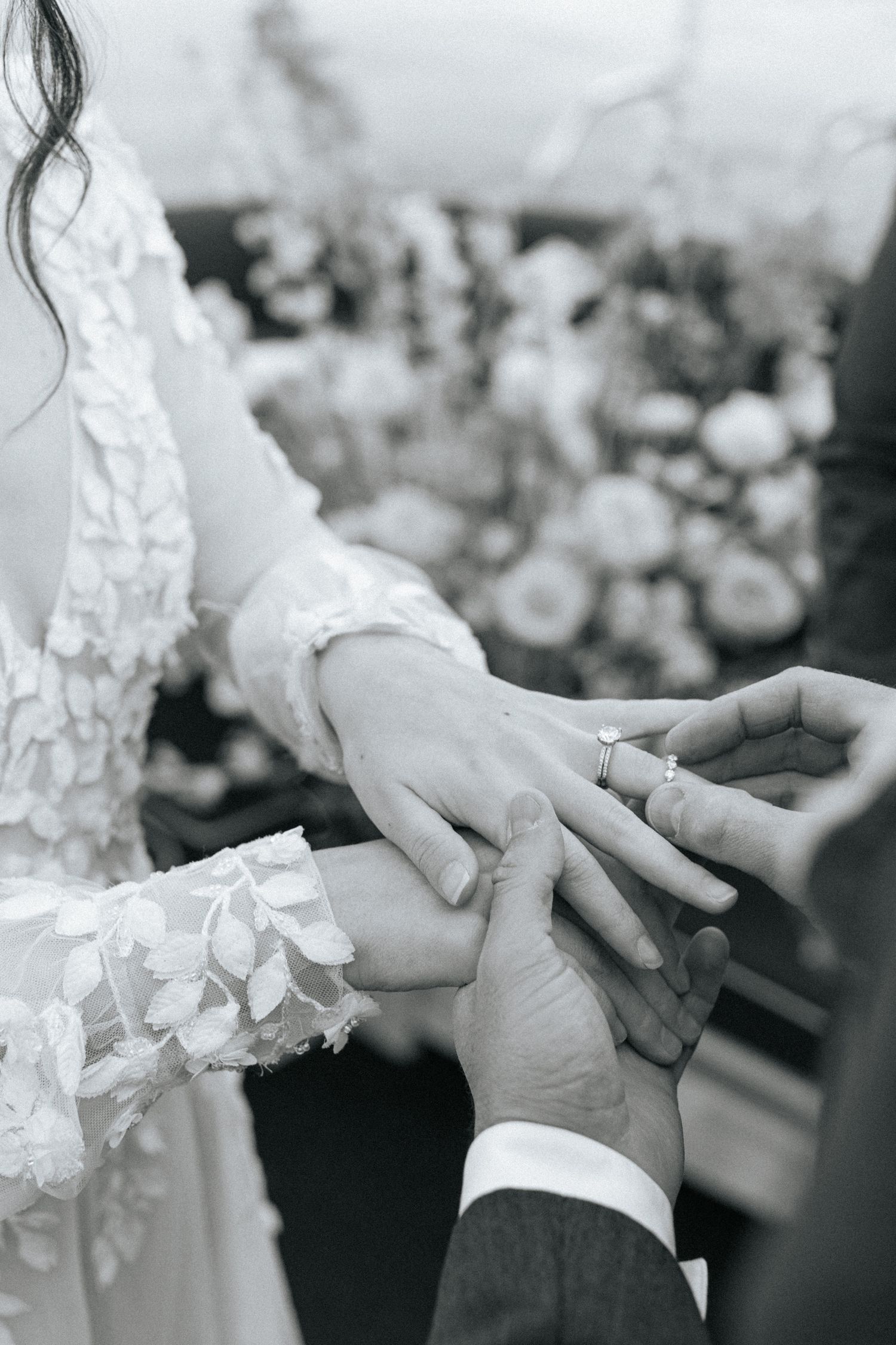 Black and white close-up of hands during a ring exchange ceremony with lace sleeve details.