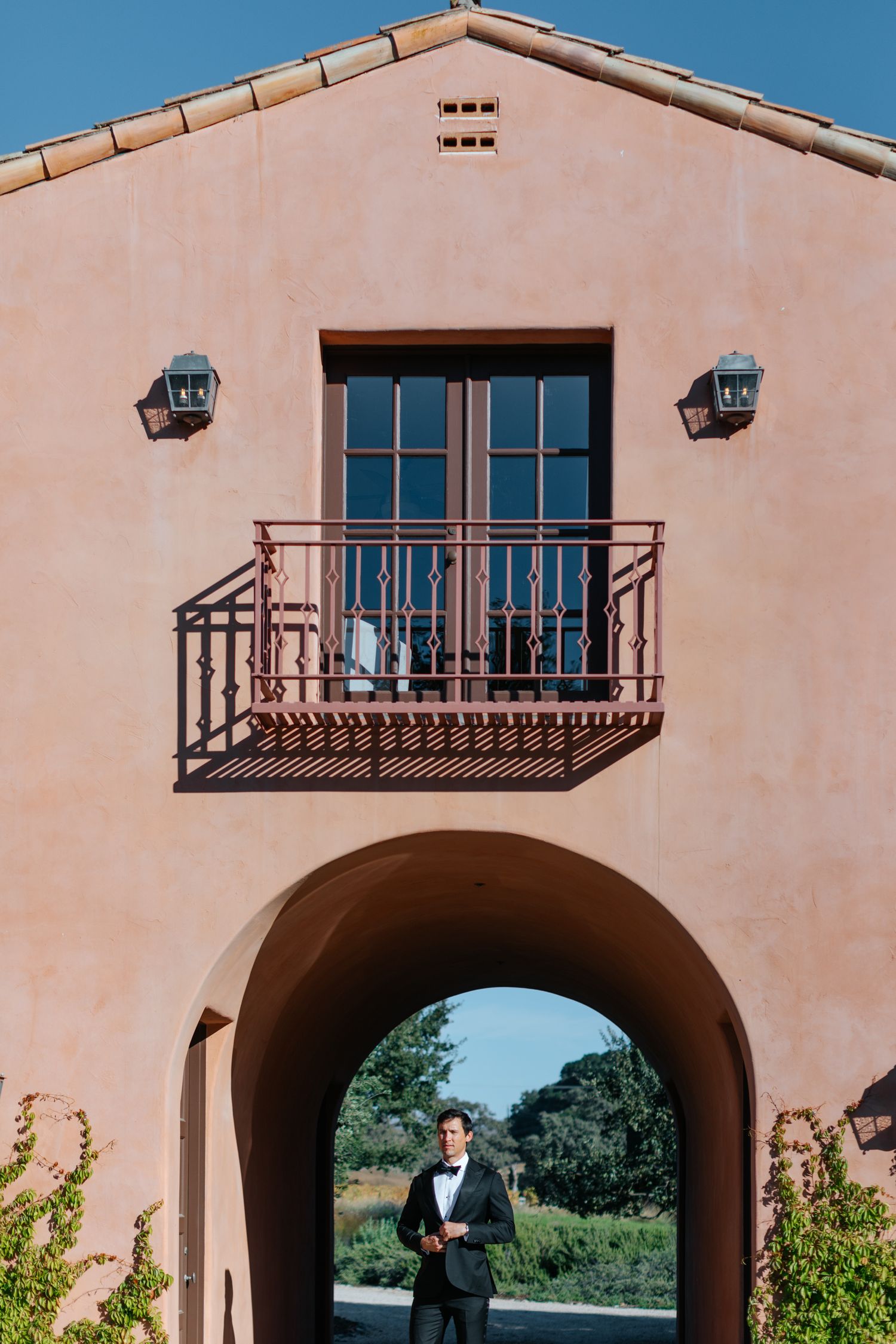Spanish colonial architecture featuring arched passageway and wrought iron balcony against pink stucco.