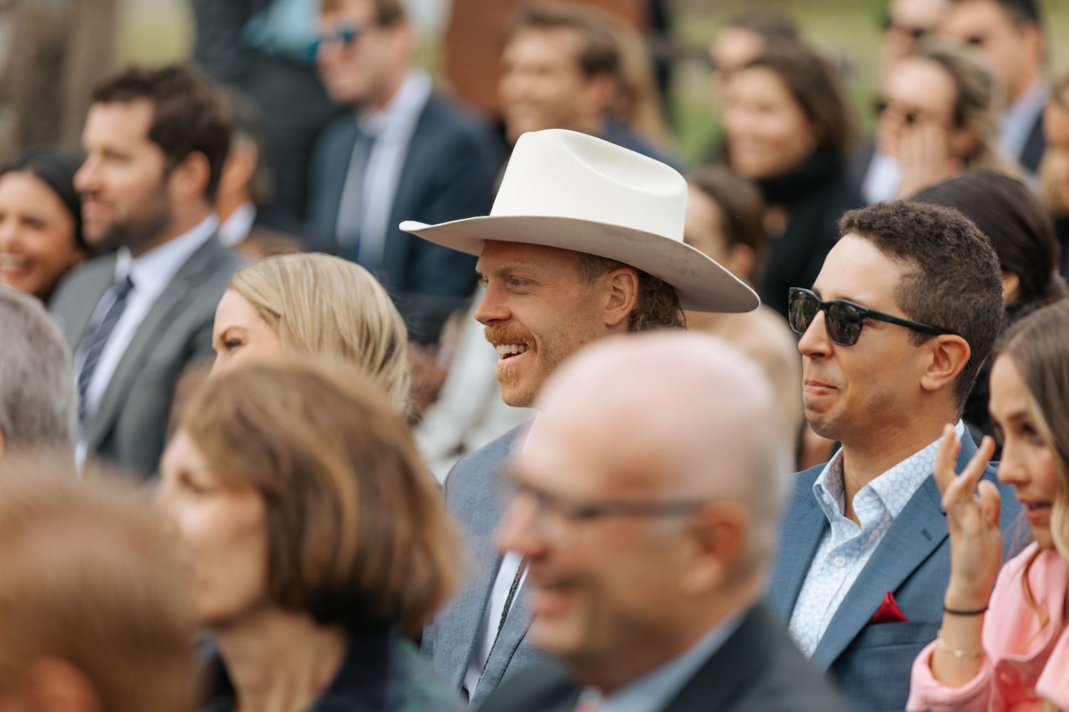 Wedding guests watch ceremony attentively in outdoor garden setting.