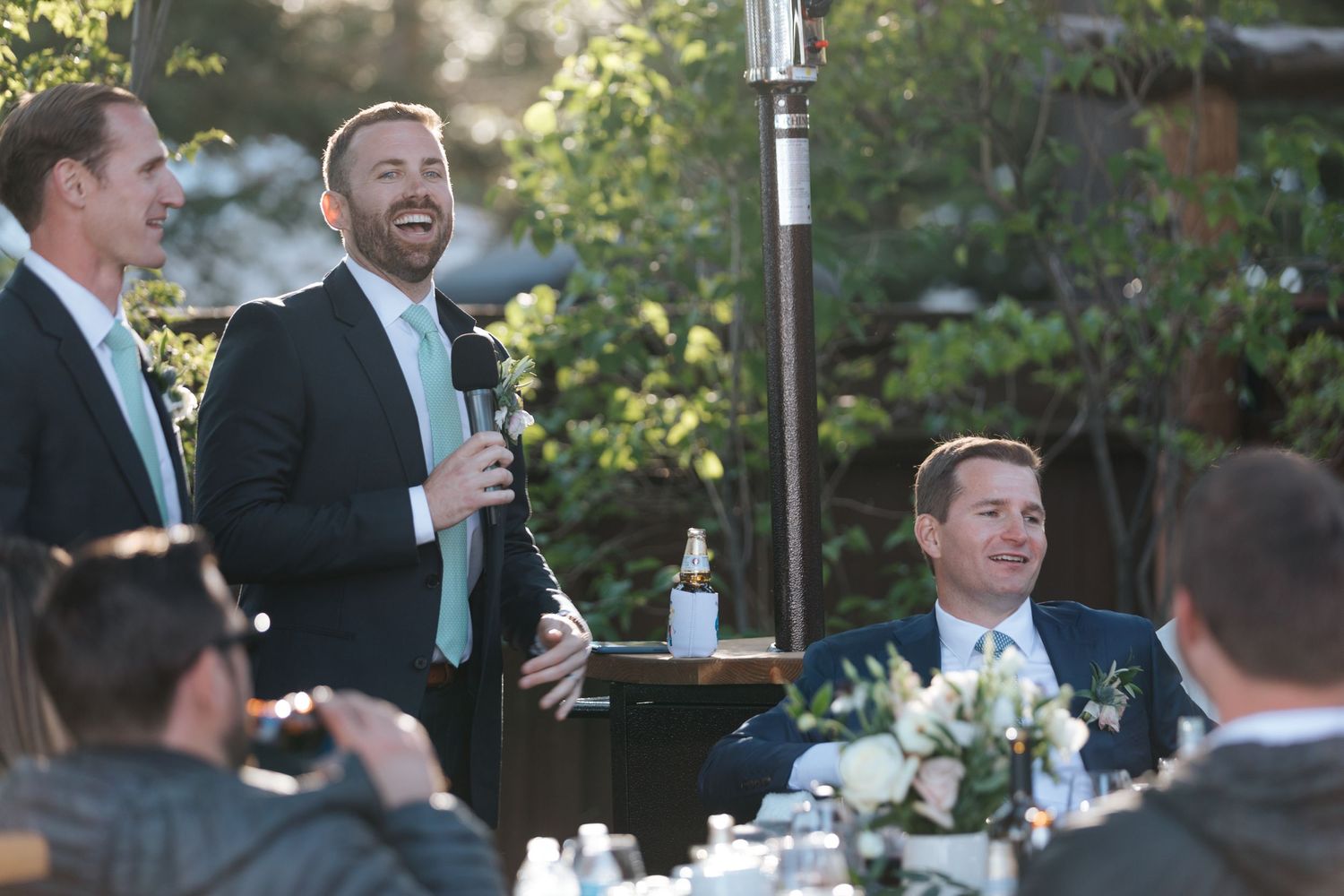 Outdoor wedding reception with guests laughing and socializing under trees.