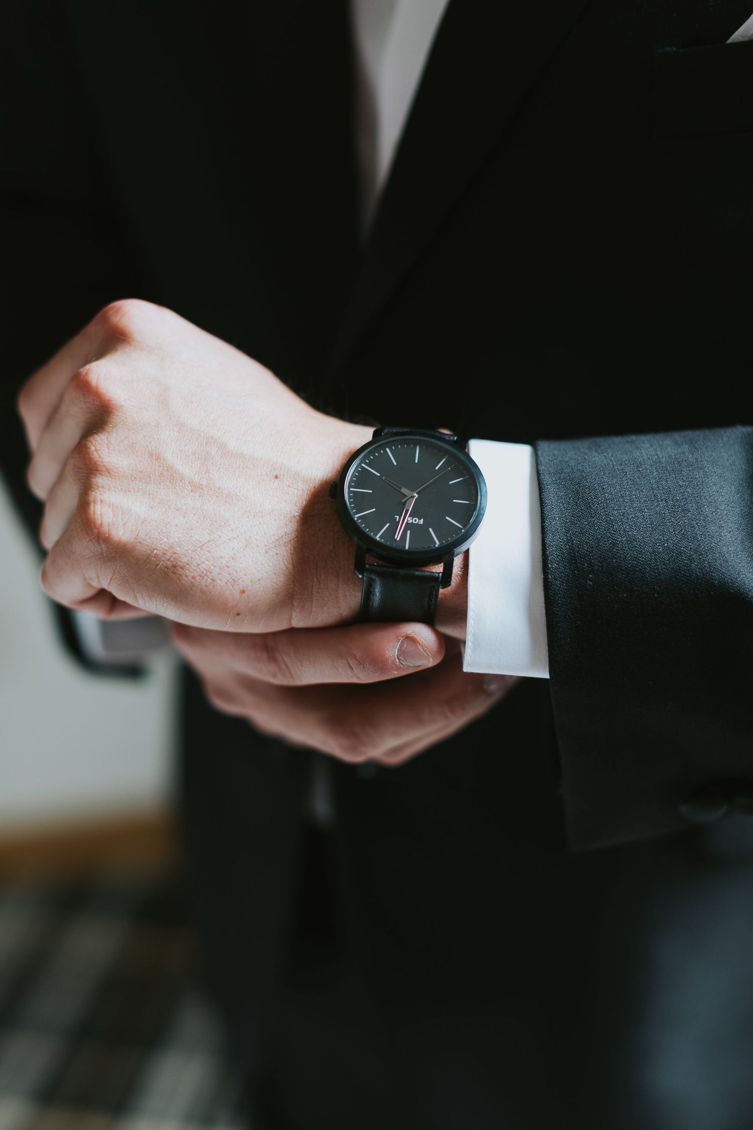 Close-up of a black minimalist watch on a formal suit sleeve.