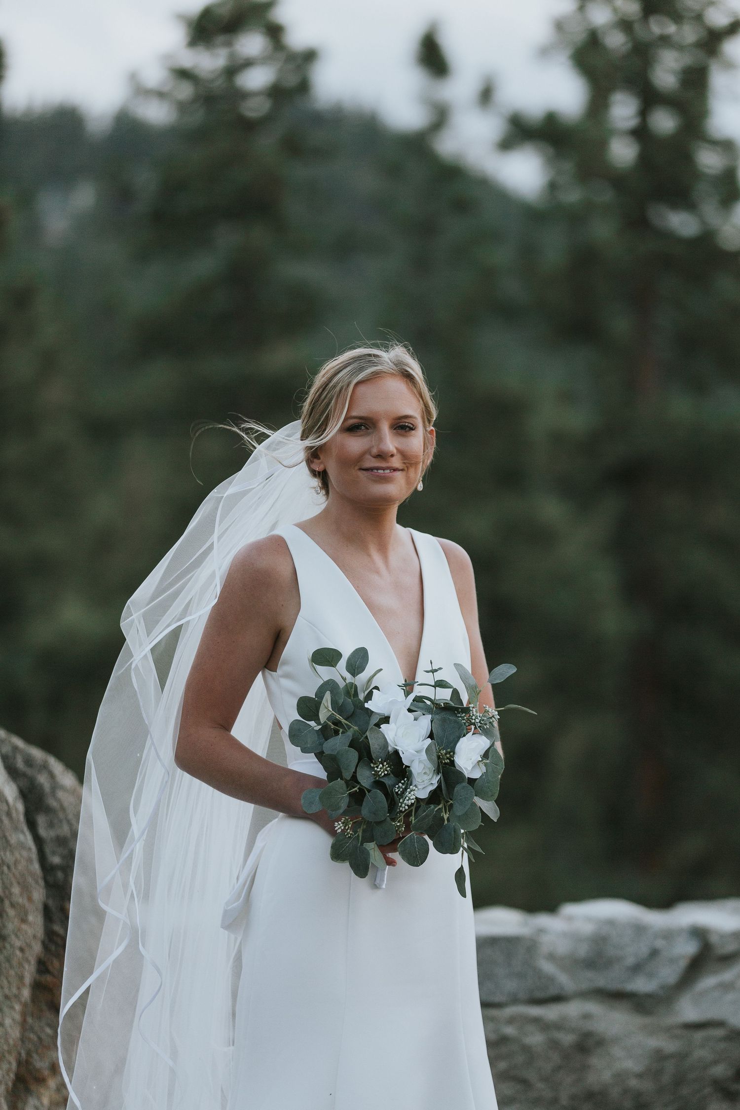 Bride holding a eucalyptus bouquet against a mountain backdrop.
