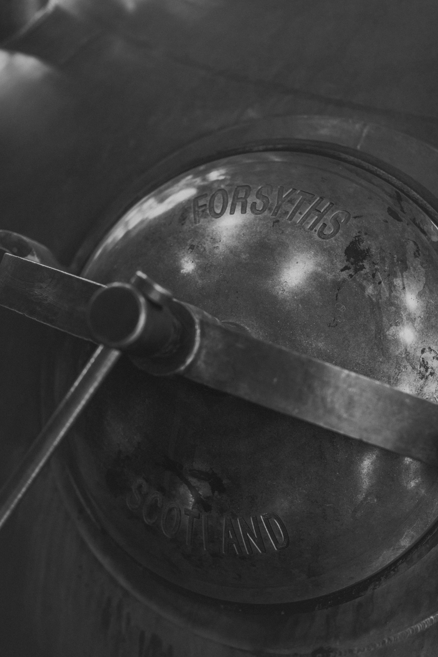 Close-up of vintage metalwork details on distillery equipment in black and white.