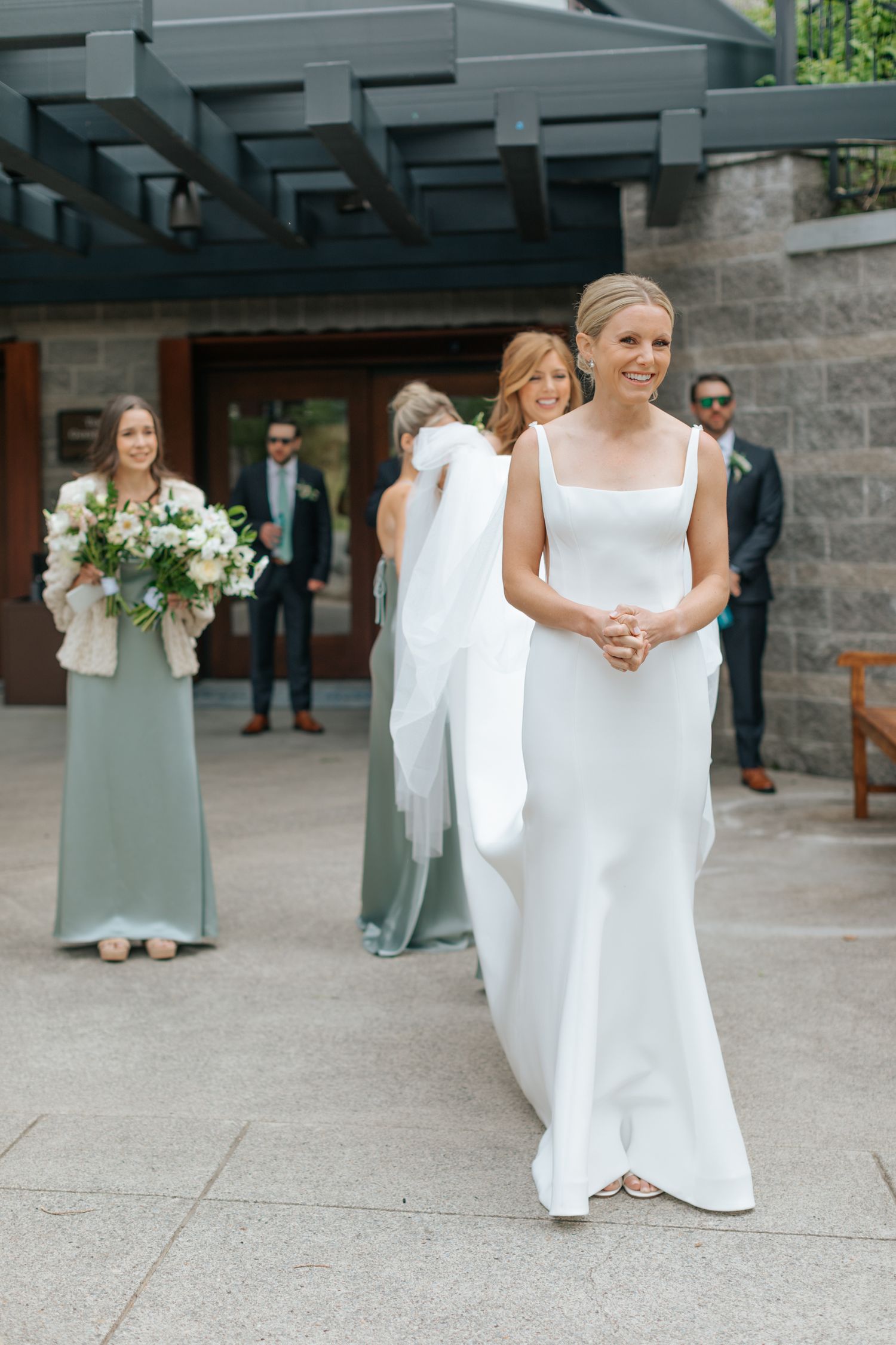 Wedding party gathered on an outdoor stone patio with bridesmaids in sage green dresses.