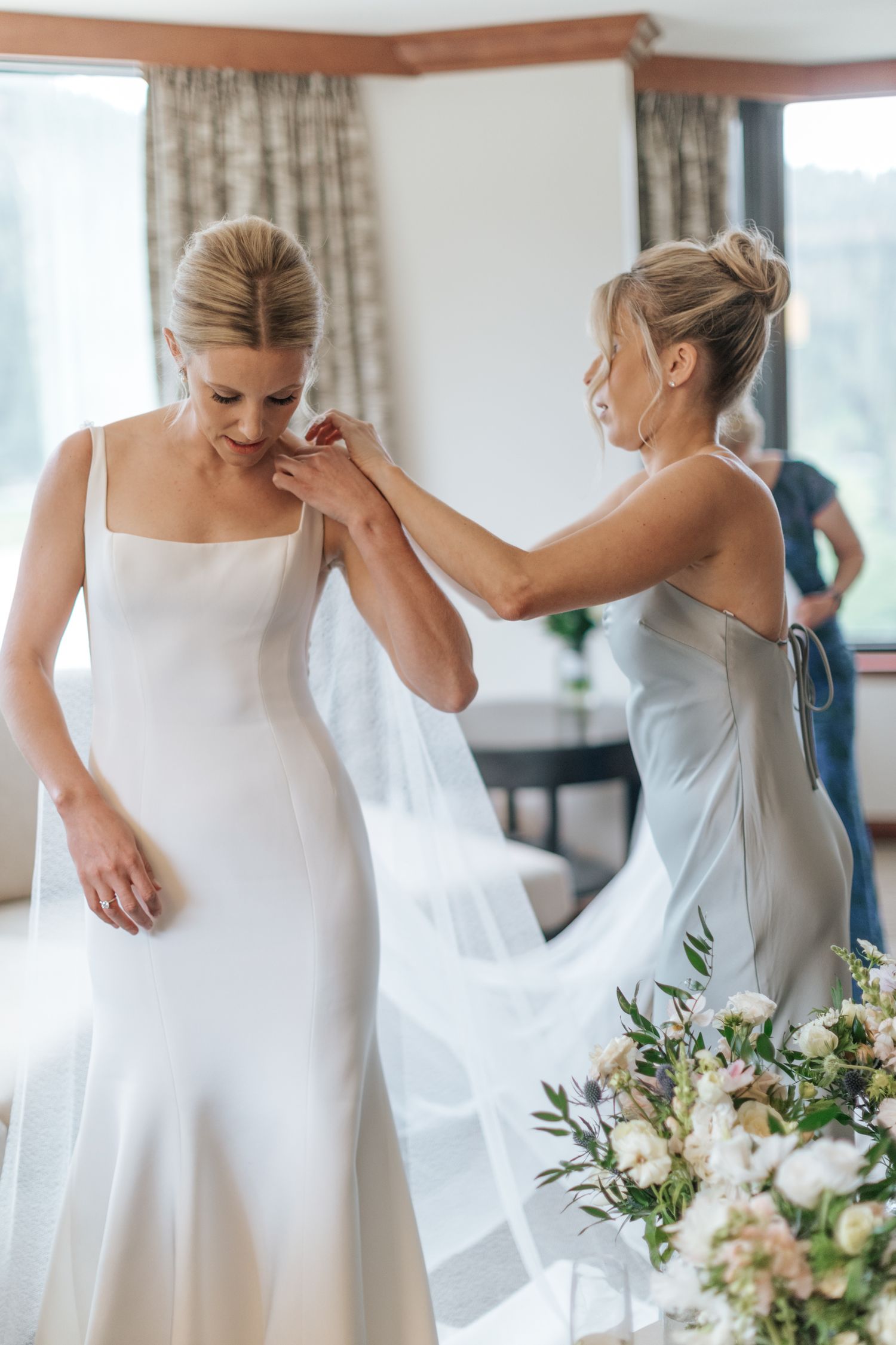 Bride getting ready in elegant white dress while holding bouquet indoors.