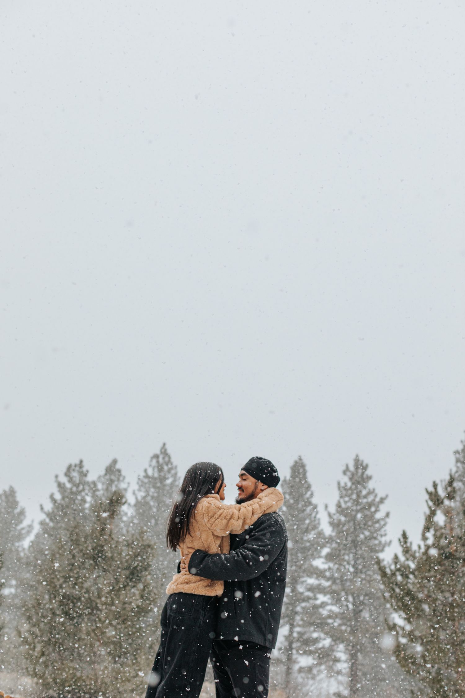 Couple embracing in a snowy forest setting during winter.