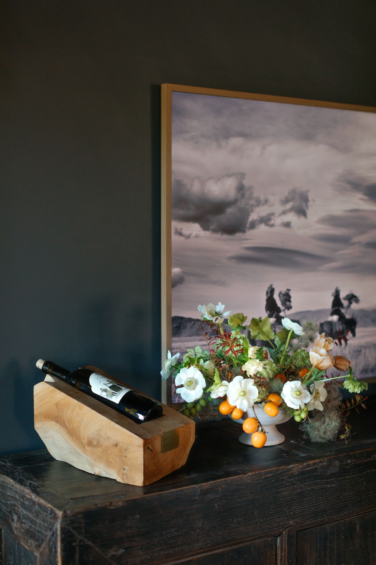 Rustic wooden boxes filled with flowers and wine bottles on dark table with dramatic sky backdrop.