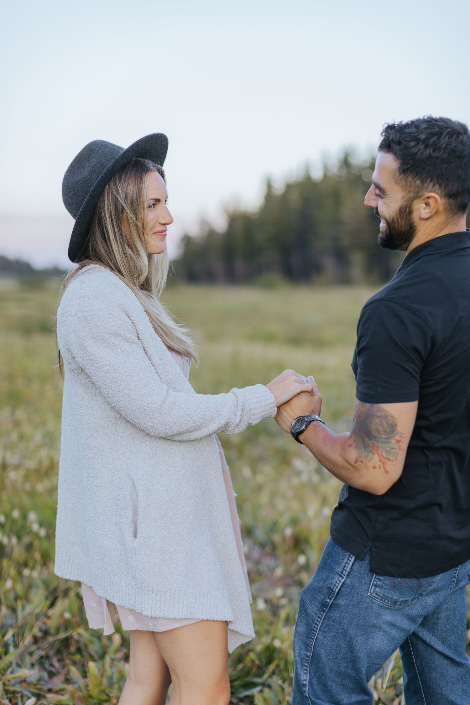 A couple shares a tender moment in a field during an engagement photo session in casual attire.