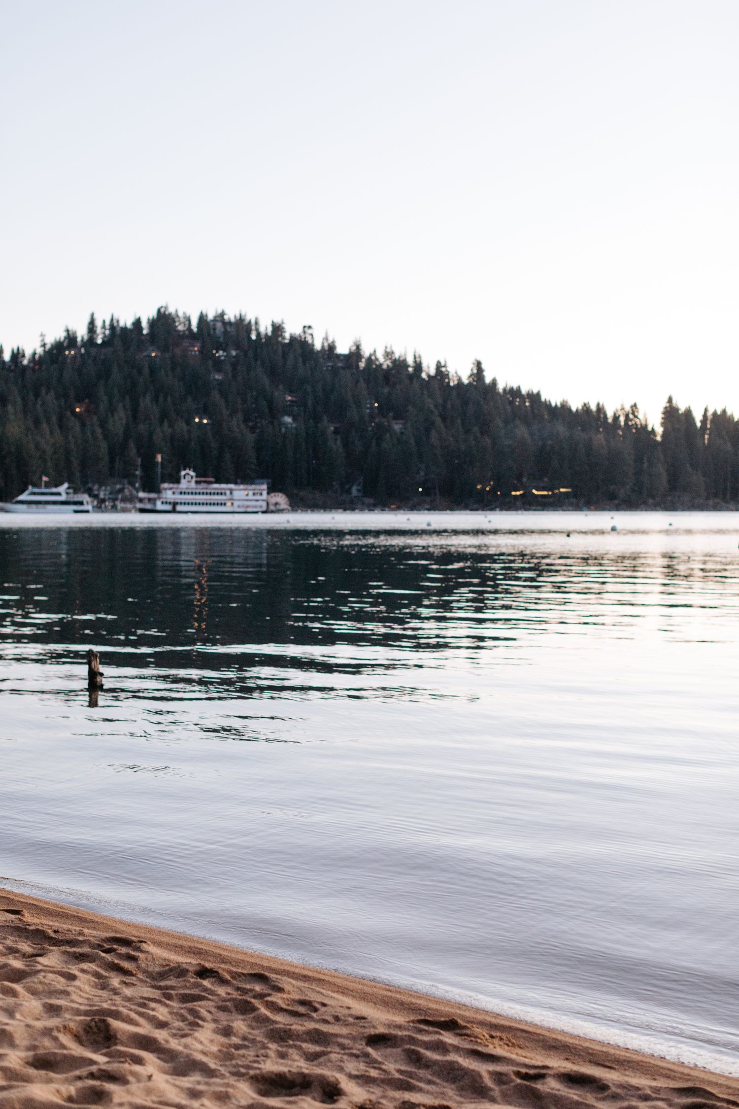 Scenic view of Lake Tahoe with pine-covered shores and boats in the distance during sunset.