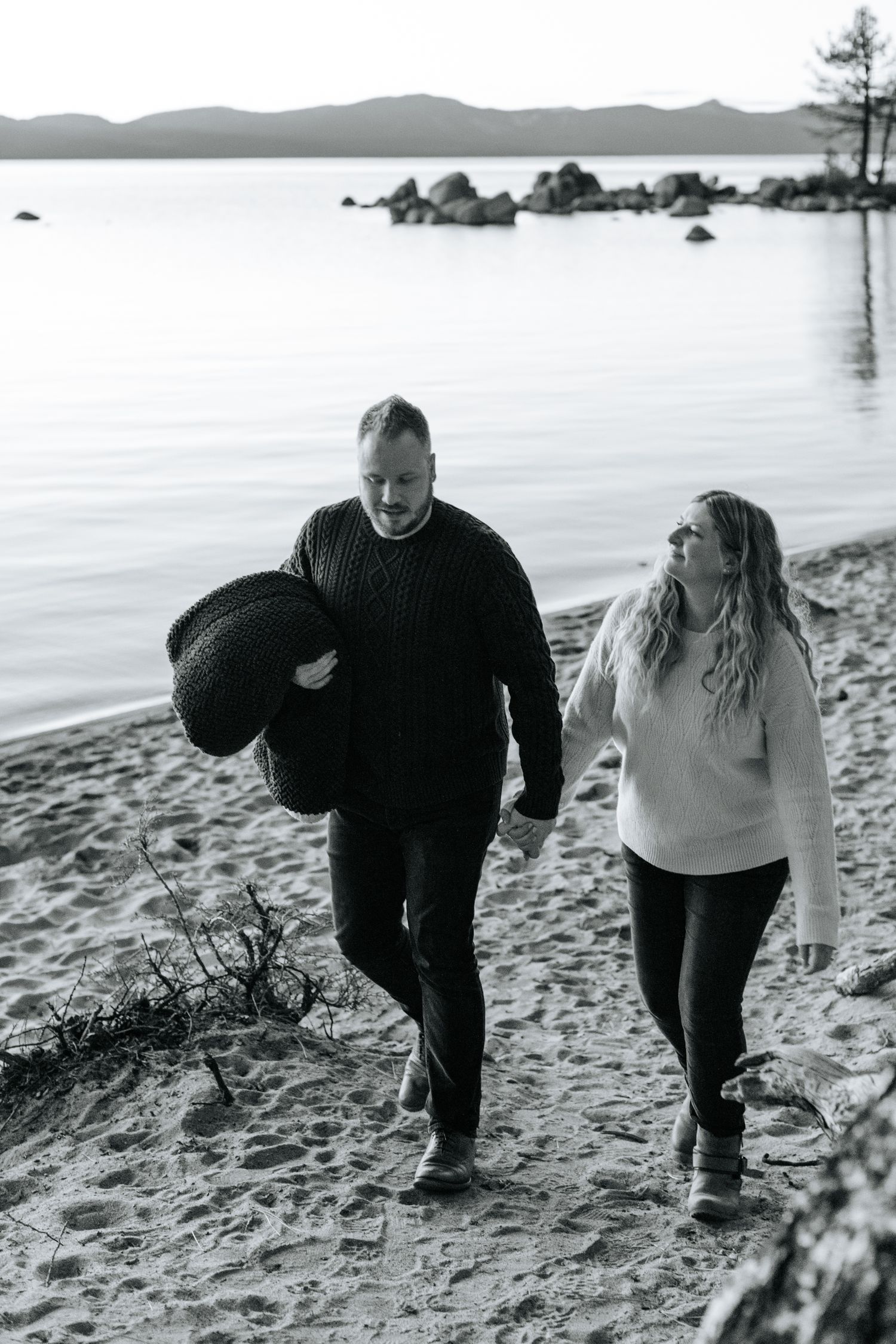 Black and white beach photos showing couple walking along shoreline with mountains in distance.