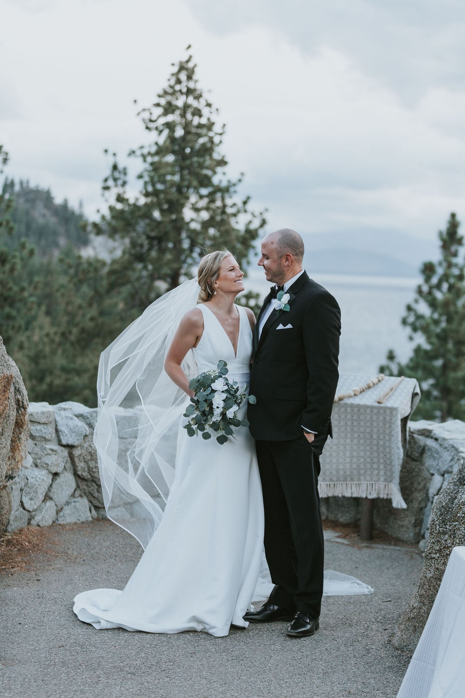 A romantic wedding couple shares intimate moments on a scenic mountain overlook with a flowing white veil.