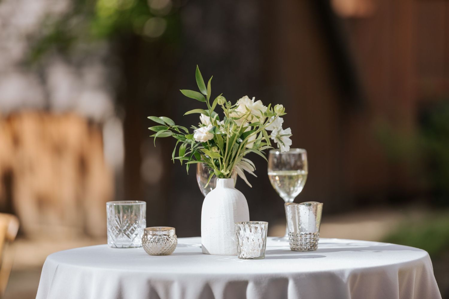 Elegant table settings with white linens and floral centerpieces at outdoor reception.