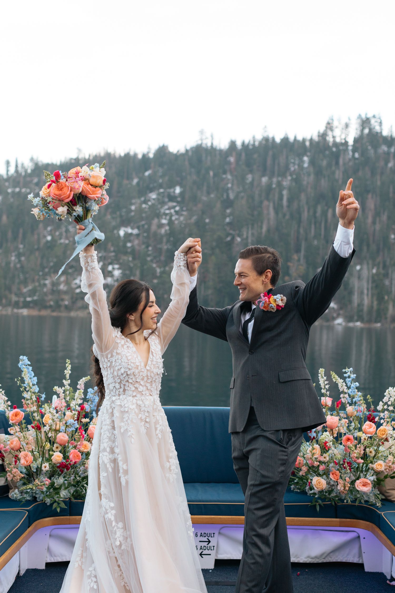Joyful newlyweds celebrating with raised arms on boat deck.