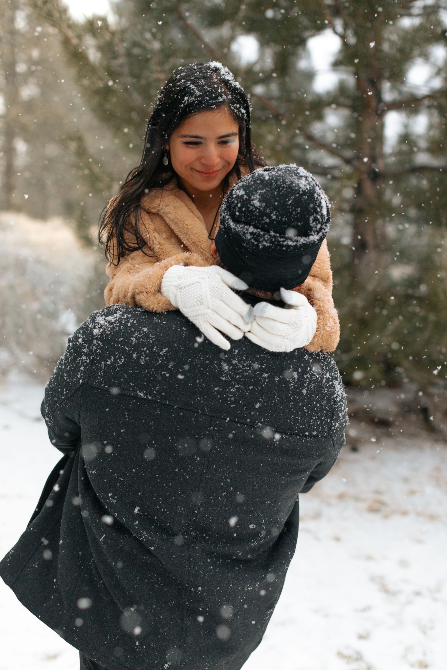 Couple sharing an embrace during a winter photoshoot with snow falling around them.