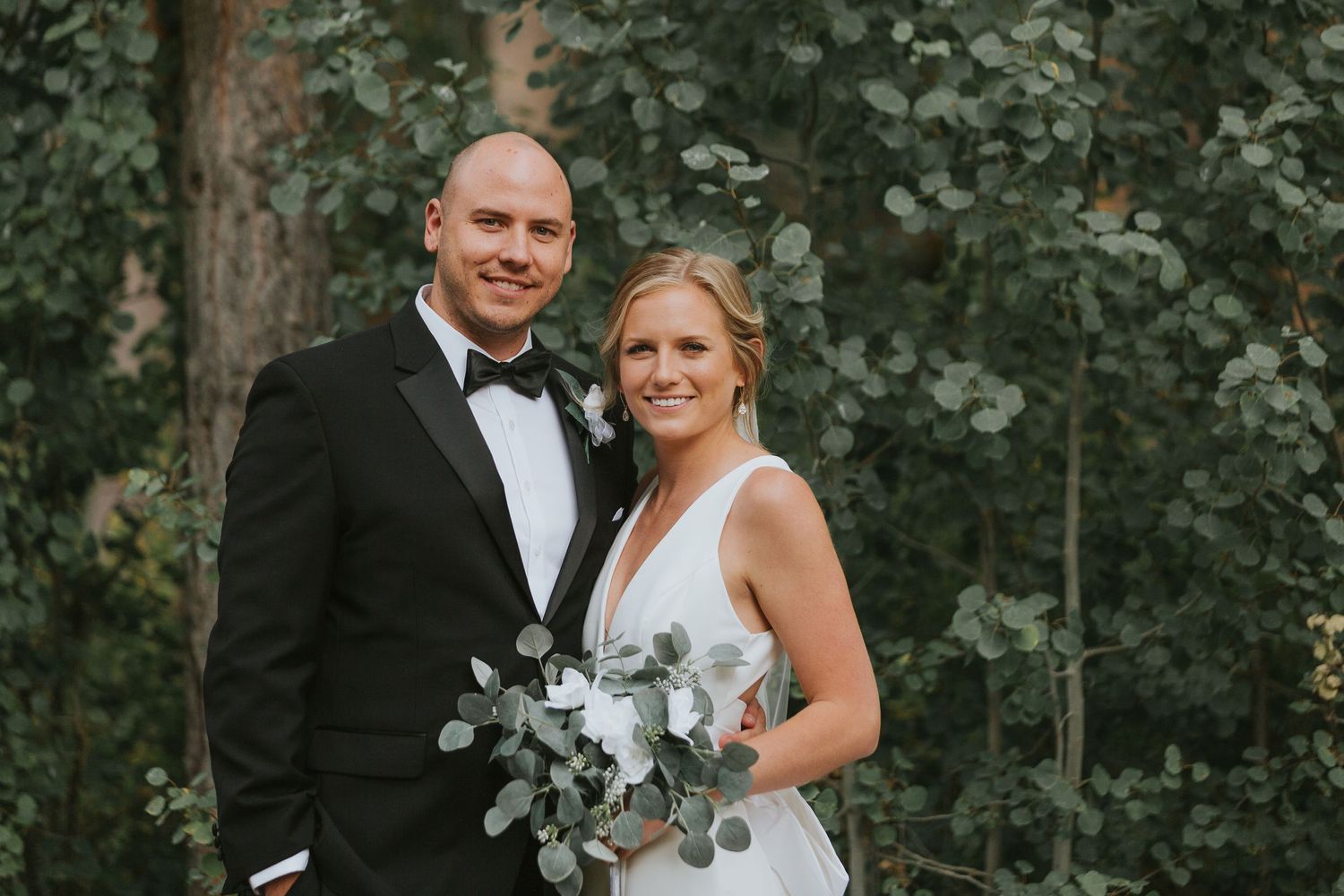 Elegant wedding couple posing in formal attire among trees.